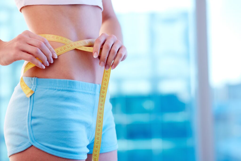 Close-up of a woman in sportswear measuring her waist